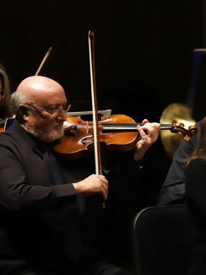 man in black shirt plays violin against black background