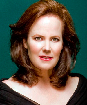 headshot of woman in black dress with v neck and short brown hair against dark green background